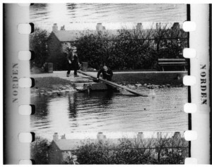 A frame from a black-and-white film showing men trying to rescue a woman from a pond